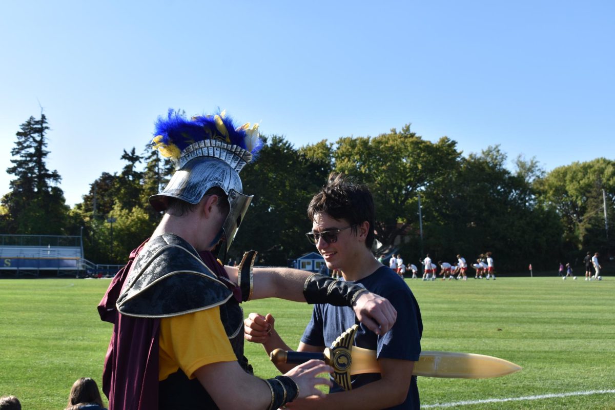 SPARTANS VS. CRUSADERS. The opposing soccer team warms up in the background as senior Lorenzo Good helps the Spartan adjust his arm band.