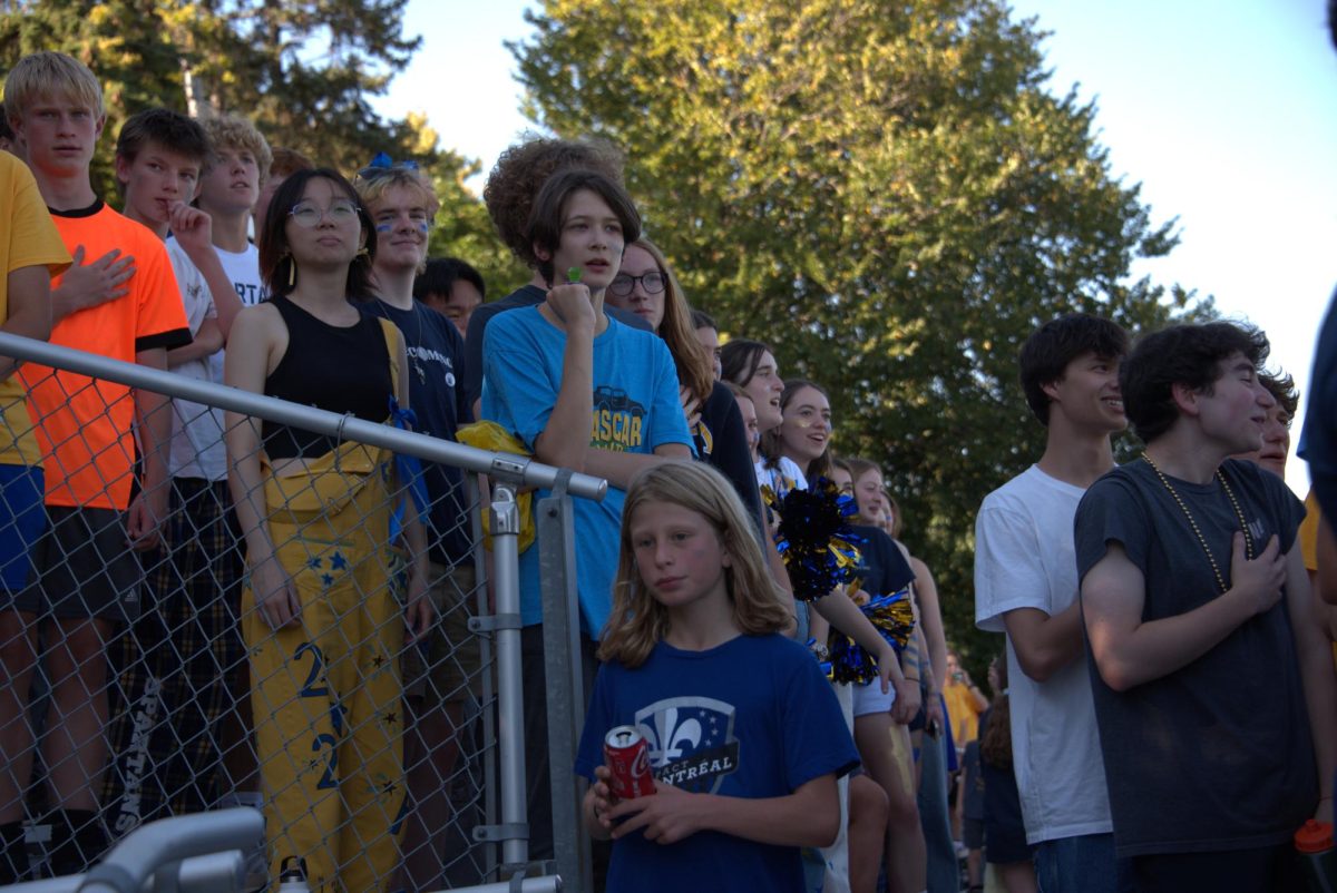 STAR-SPANGLED BANNER. Fans listen along as seniors Mia Collins, Sawyer Bollinger-Danielson and Eva Lutgen of the girls soccer team sing the national anthem before the game. 