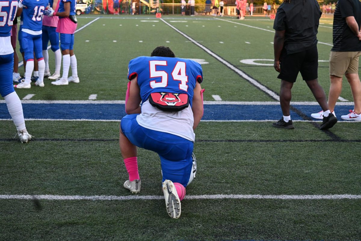 PREGAME PRAYER. Player #54 takes a knee before running onto the field and joining his team.