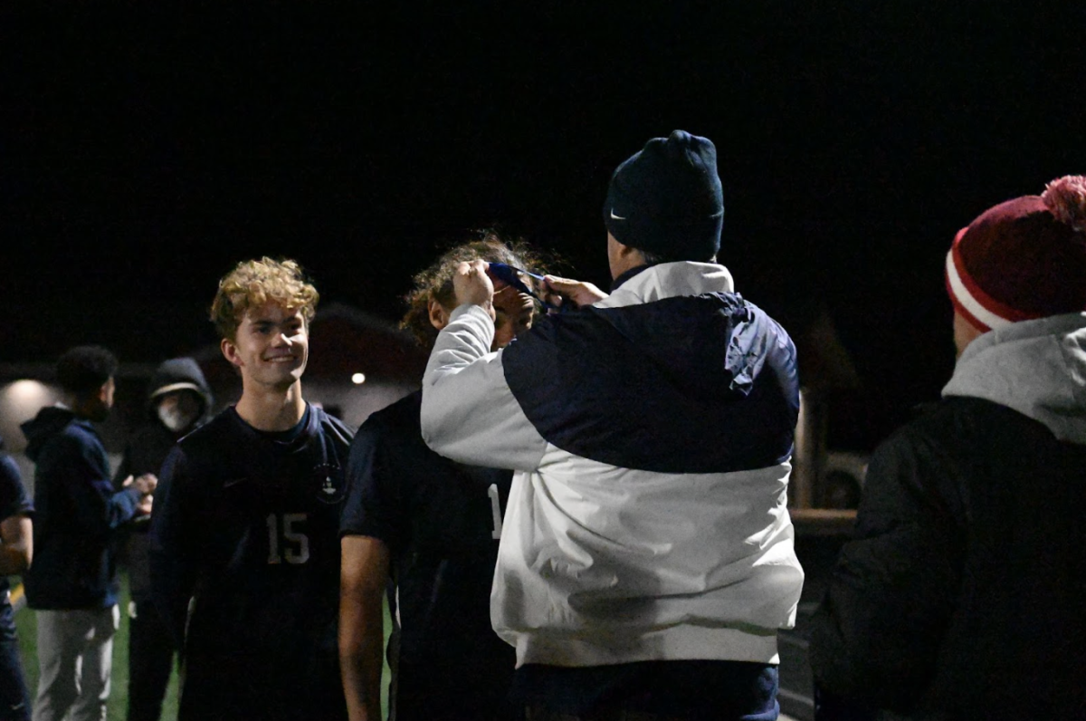 GOLDEN GAME. David Schumacher (‘25) grins as sophomore Langston Thompson, gets crowned with his championship medal by athletic director Randy Comfort.