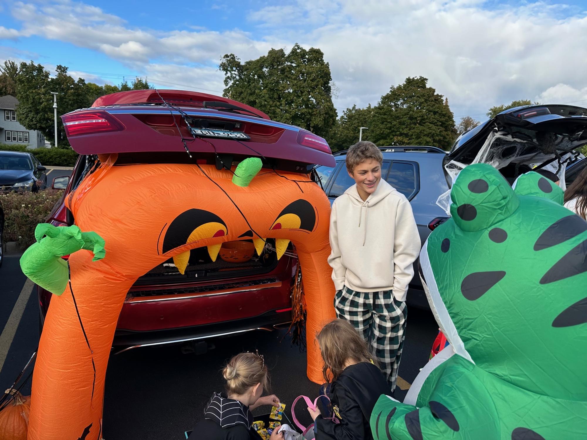 CRAZY FOR CANDY. Sophomore Brooks Geiger hands out candy to the lower schoolers with a trunk decorated with a blow up pumpkin. 